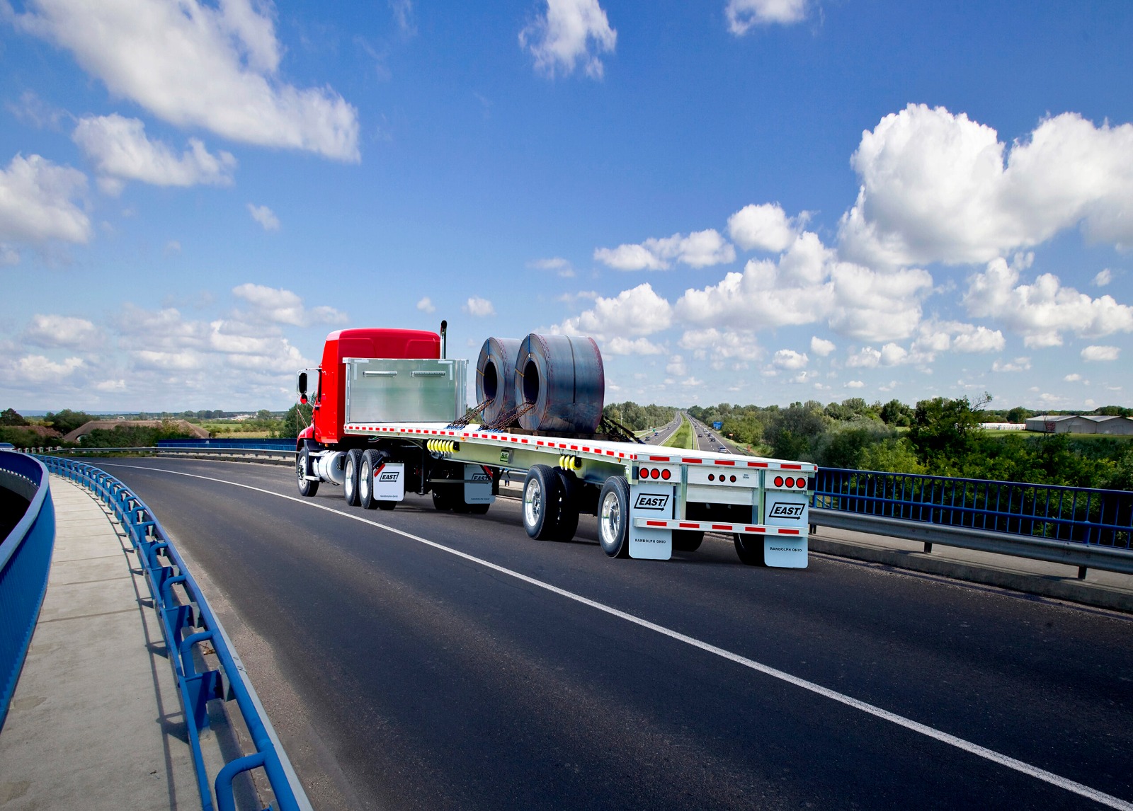 Flatbed trailer hauling steel coils across a highway bridge